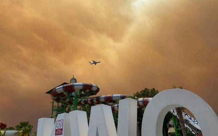 28 July 2021, Turkey, Side: Smoke drifts over leisure facilities at a hotel complex in the Turkish resort region of Antalya as a plane is on approach to land. Winds drove flames from several wildfires toward residential districts, the district administrator of Manavgat told CNN Turk. Photo: Cevin Dettlaff/dpa-Zentralbild/dpa 28 July 2021, Turkey, Side: Smoke drifts over leisure facilities at a hotel complex in the Turkish resort region of Antalya as a plane is on approach to land. Winds drove flames from several wildfires toward residential districts, the district administrator of Manavgat told CNN Turk. Photo: Cevin Dettlaff/dpa-Zentralbild/dpa