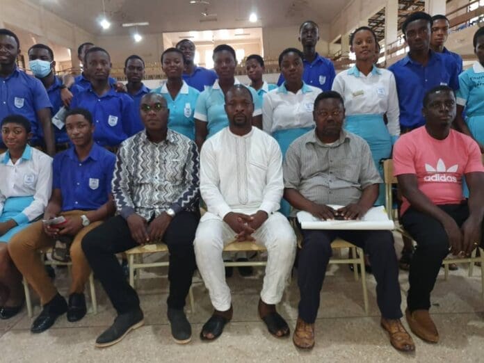Alhaji Quandah speaking to the students and also in the middle, flanked by some staff of the secretariat with some students behind.